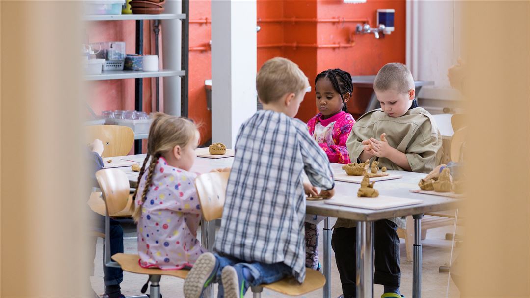 Vier Kinder modellieren konzentriert Tonfiguren an einem Tisch.
