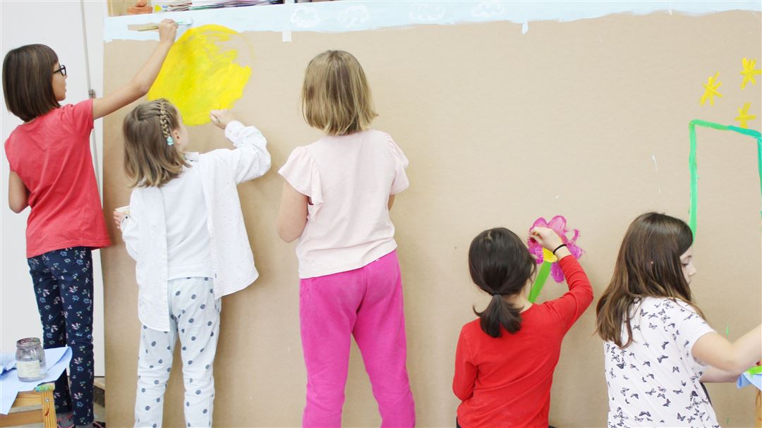 Fünf Kinder malen gemeinsam ein grossformatiges Wandbild auf braunem Papier.
